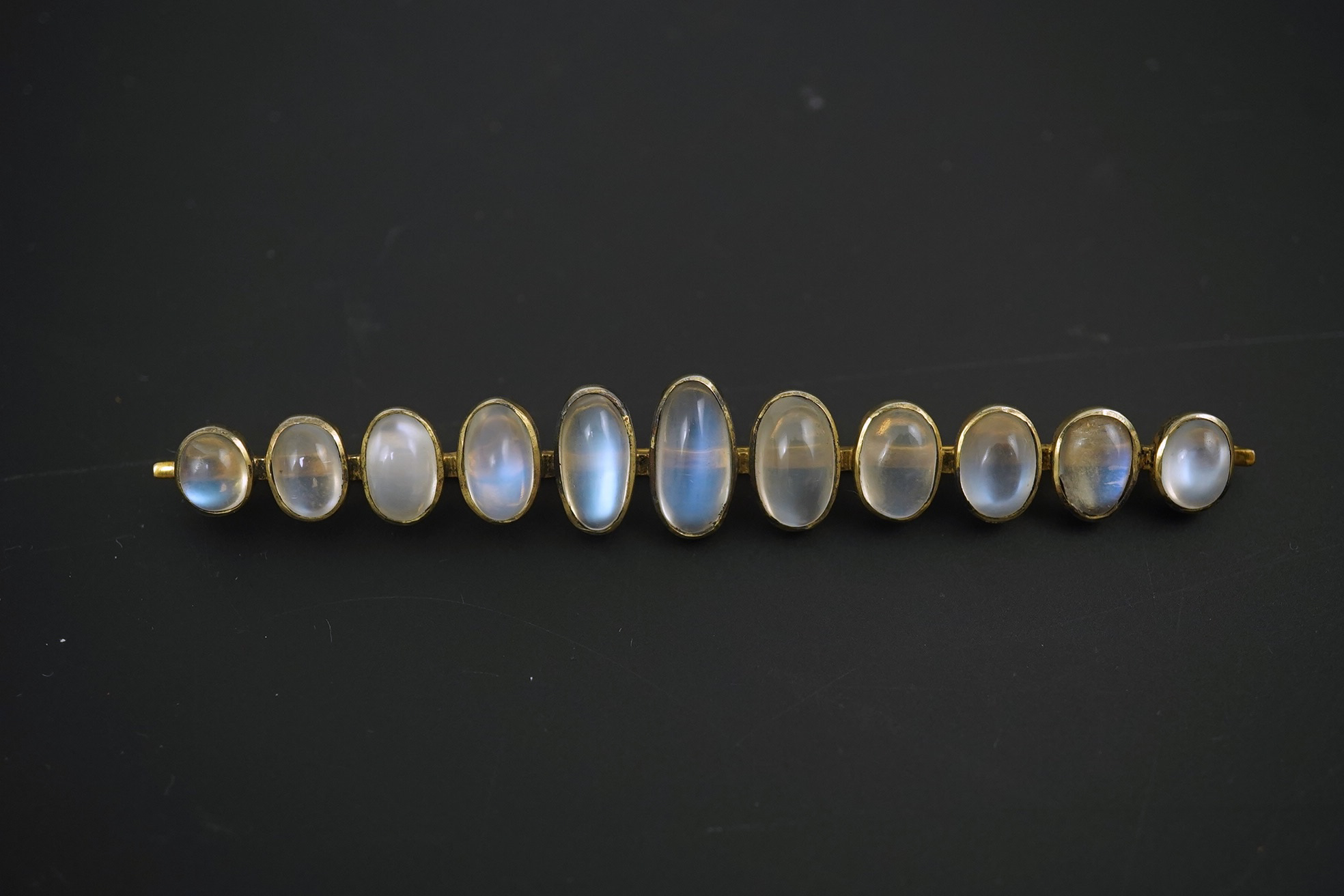 A gold and eleven stone graduated cabochon moonstone set bar brooch